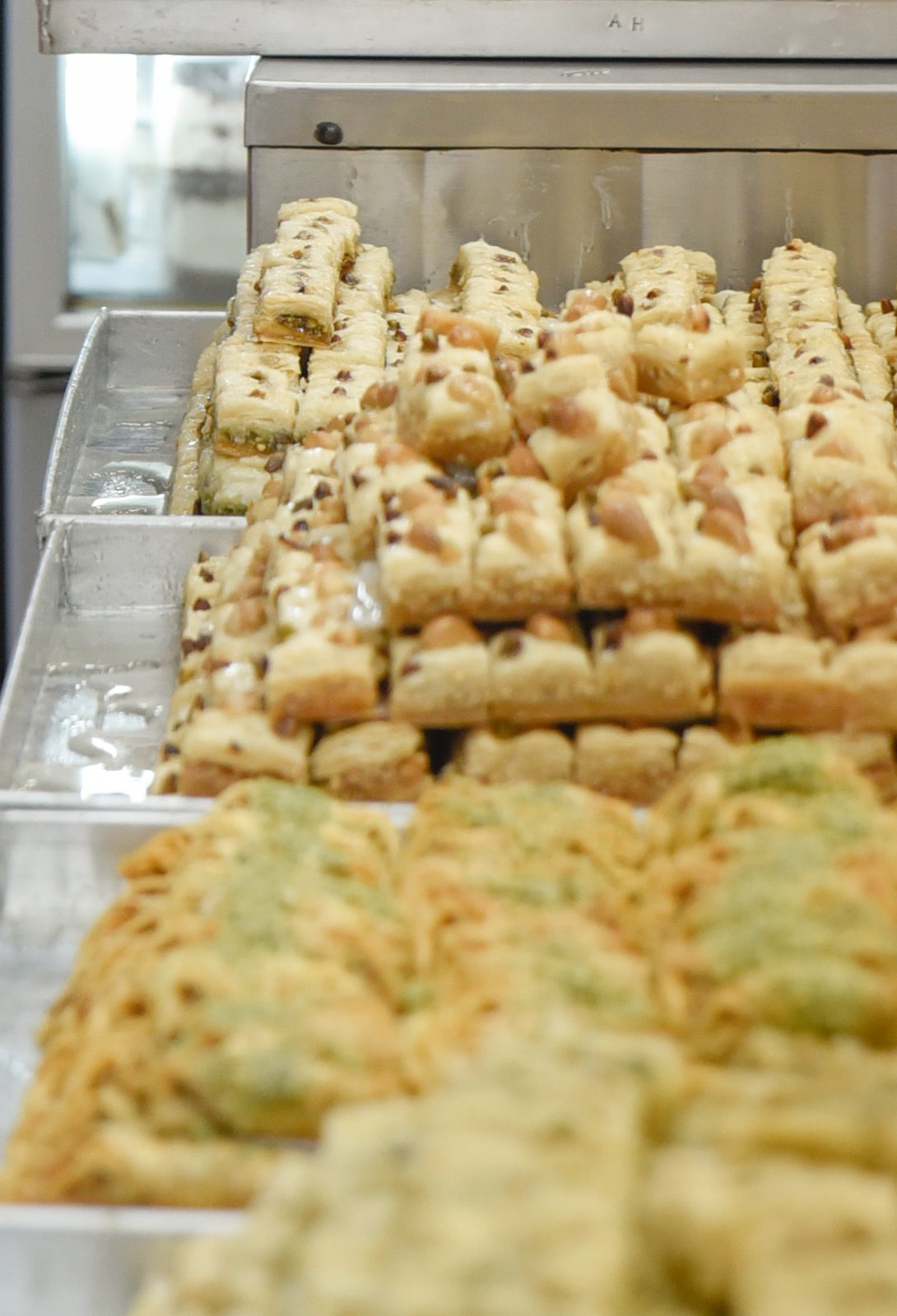 Trays of nut baklava stacked in tiers at Abd al-Hadi Sweets, with pistachio rolls in front